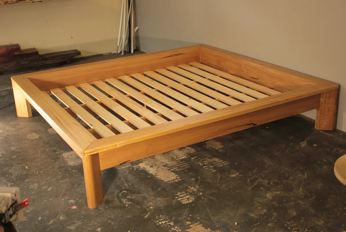 A solid timber bed frame with an integrated headboard and a slatted base